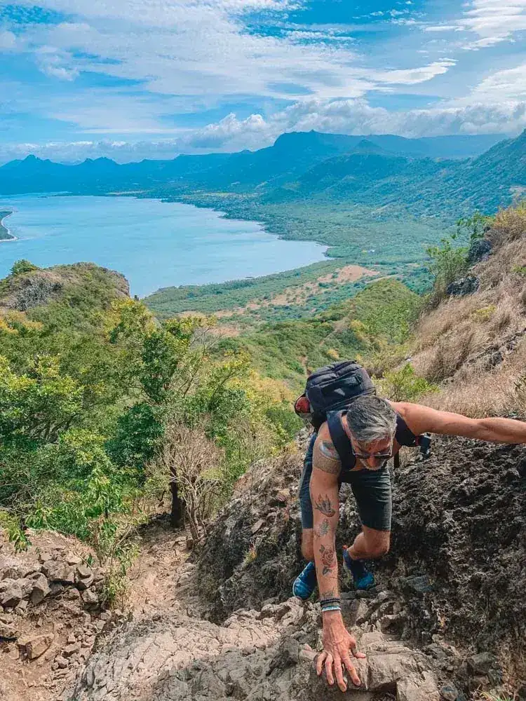 Hiker climbing a rocky trail with a lagoon view below